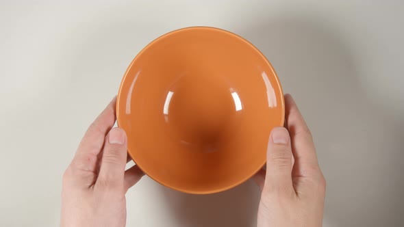 Human Hands Puts A Orange Soup Bowl On A White Table