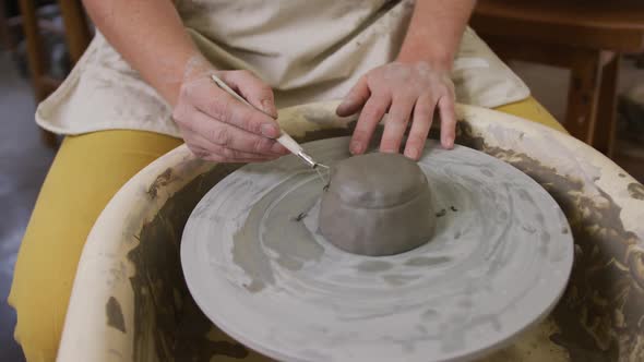 Mid section of female potter using loop tool for finishing pottery at pottery studio alt
