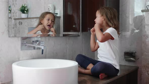Little Cute Girl Brushes Her Teeth with Dental Floss in Front of the Mirror