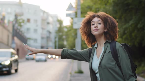 Beautiful African American Millennial Woman in Casual Wear Waving Down Car Hitchhiking on Roadside alt