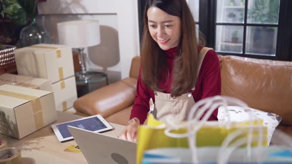 Happy Asian female shop owner checking customer order on digital tablet