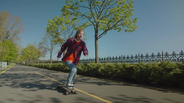 Skillful Hipster Female Skateboarder Riding on Longboard in Public Park alt