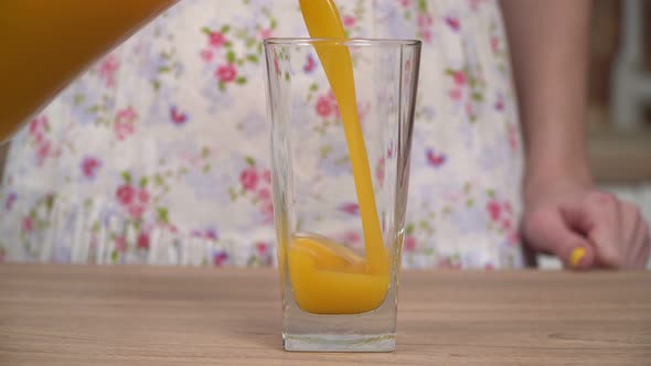 A Woman in the Kitchen Pours Fresh Juice From a Jug Into a Glass alt