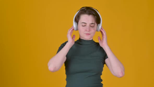Young girl with headphones listens to music and dances isolated on yellow background