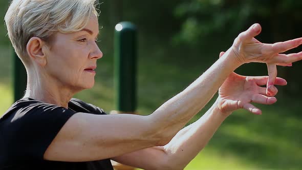 An Elderly Woman Does a Warmup in the Park on the Playground alt