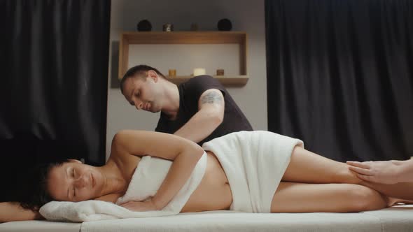 Slim Brunette Woman Receiving Body Rejuvenating Massage Procedure in Spa Pair of Massage Therapists alt