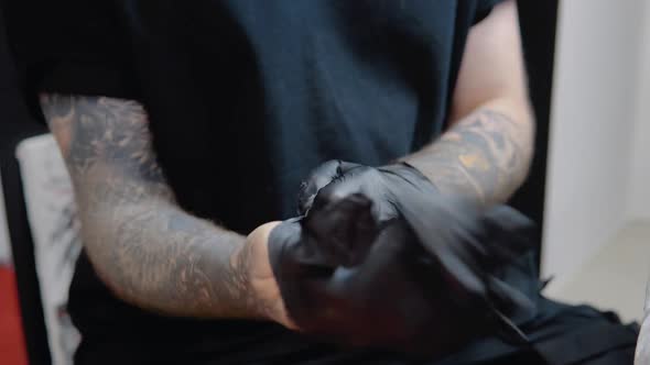 Tattoo Master with Tattooed Hands Wears Sterile Gloves and Disinfects His Hands Before Working with alt