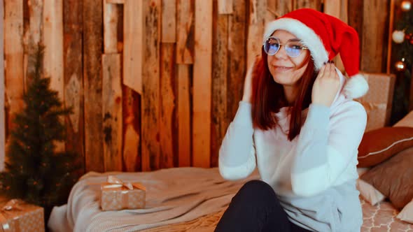 Young Woman in Santa Hat and Glasses Preening Herself in Front of Camera alt