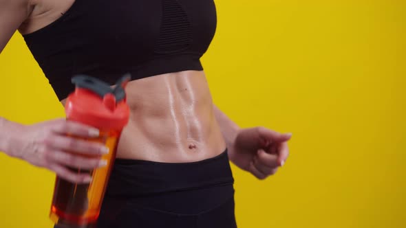 Woman Holds a Sports Shaker with Water in Hand and Shows the Muscles of the Abdomen Closeup alt