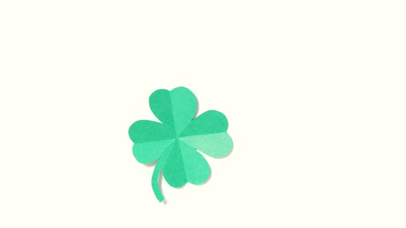 A leaf of clover cut out of paper is spinning on a shiny green background. alt
