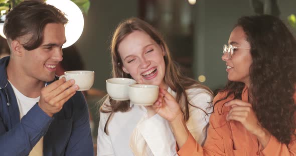 Millennial People Cheering with Cups and Laughing While Sitting in Modern Cafe. Young Smiling alt