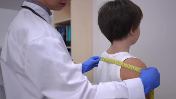 Unrecognizable Doctor Measuring Shoulders and Head of Caucasian Boy in Hospital alt