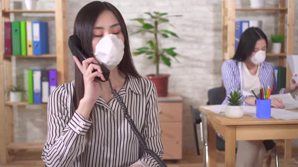 Two Young Asian Girls Office Workers in Protective Medical Masks on Their Faces alt