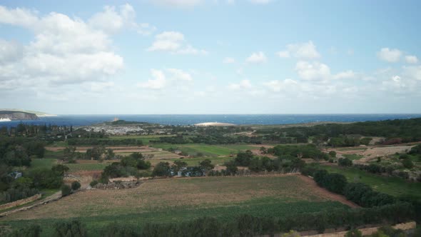 AERIAL: Revealing Part of Comino Island and Farmlands with Village in Background alt