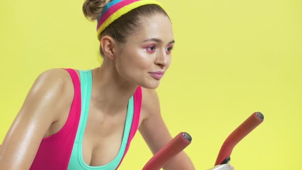 Portrait Closeup of Pleased Adult Girl Wearing Colorful Sportswear Pedalling on Training Simulator alt