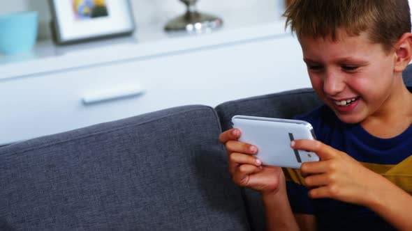 Boy using mobile phone while upset sister sitting besides him in living room alt