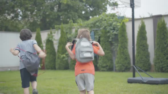 Back View Wide Shot of Cheerful Schoolboys Running Home and Throwing Up Backpacks. Joyful Caucasian alt