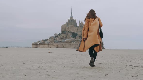 Rear View Zoom in on Fashionable Tourist Woman Slowly Walking on Sea Sand at Epic Mont Saint Michel alt