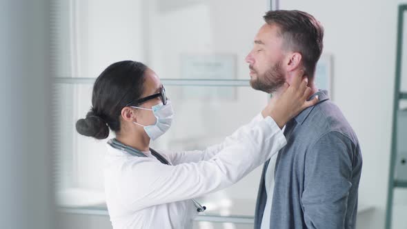 Female Doctor in Mask Examining Neck and Throat of Male Patient alt