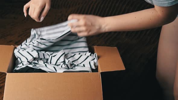 Young Girl Disassembles a Parcel With Things and Examines Clothes alt