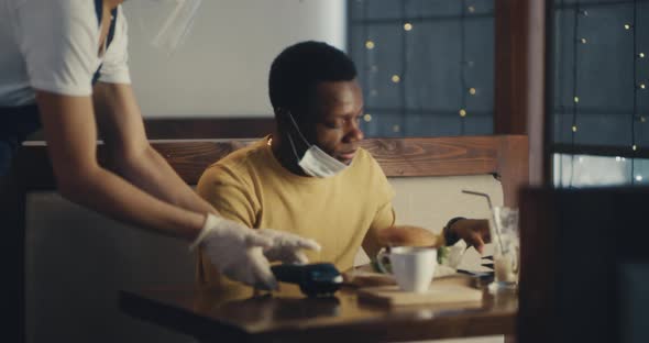 Black Man in Medical Mask Paying with Card for Cafe Meal alt