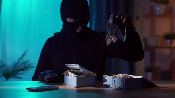 Portrait of a Robber in a Balaclava with Jewelry in His Hands alt