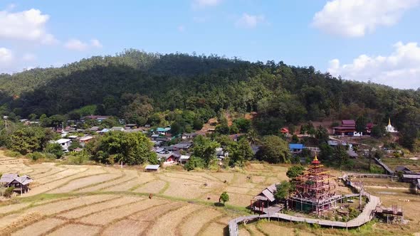 Aerial of a Tropical Mountain Town and Rice Paddies with a Buddhist Temple Under Construction alt