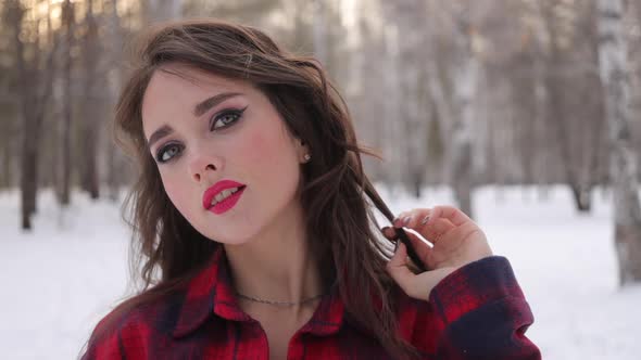 Young Woman with Wavy Hair Standing and Touching Face in Winter Forest