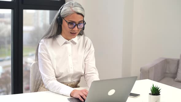 Confident Aged Woman with Headset Wrinkles on the Face Consulting the Client Online
