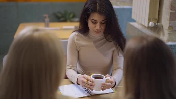 Concentrated Middle Eastern Woman Drinking Tea Writing in Sketchpad Sitting on Break with Colleagues alt