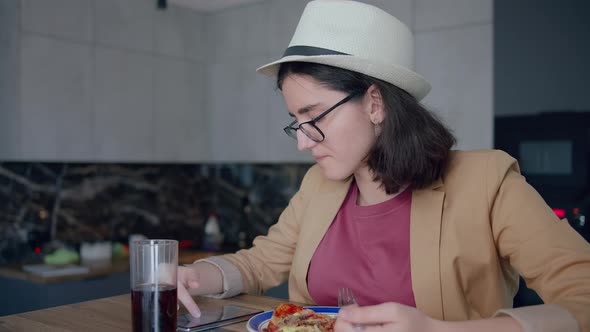 Portrait of a Pretty Girl in a Hat and Glasses Eating and Browsing a Mobile App alt
