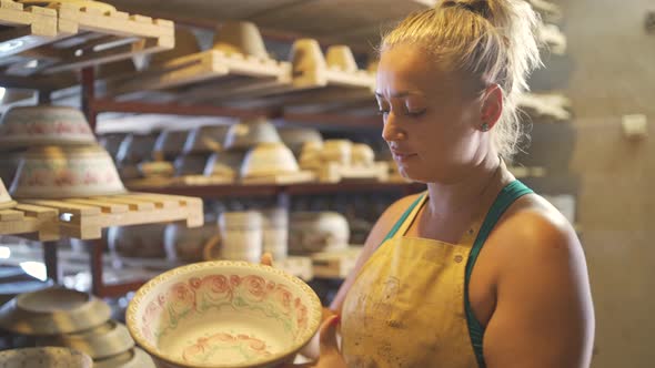 Woman Potter Artist Taking Big Clay Bowls Off of Wooden Rack in Pottery Workshop alt