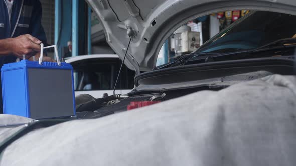 Young mechanic changing and fix battery in car with in the garage, auto service.