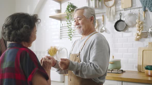 Asian mature senior couple is dancing and smiling in kitchen at home. alt