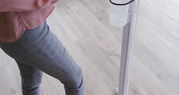 Businesswoman using foot pump sanitizer to disinfect hands as she enters the workplace alt