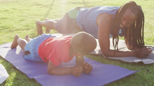 Video of happy african american son and father doing plank on grass on sunny day alt