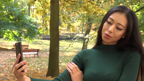 A Young Asian Woman Takes Selfies with A Smartphone in A Park
