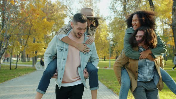 Joyful Young Men Giving Piggyback Ride To Happy Women Having Fun in Park alt