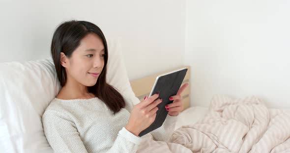 Woman reading on tablet computer and sitting on bed alt