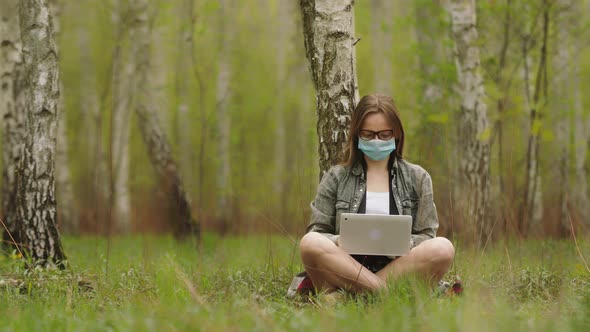 Freelancer During Quarantine in the Nature. Woman in Mask Is Working on Laptop in Forest alt