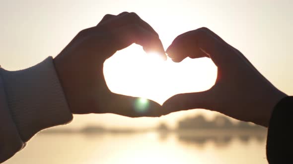 Hands of Men and Women Came Together and Show Form the Symbol of a Heart Shape at Sunset alt