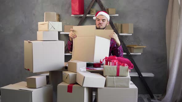 Portrait of a Bearded Guy Santa Claus in a Hat Works in a Warehouse of an Online Store Prepares alt