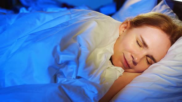 a Woman with Red Hair Sleeps on Her Side in Bed and Sees Quiet Dreams Smiles alt