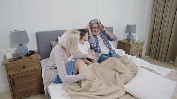 Cute Little Girl Granddaughter Listening Music with Grandparents While Relaxing Together in Bed alt