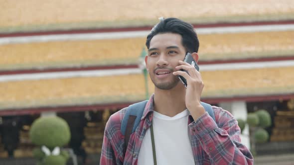 Attractive solo tourists Asian man walking and talk to mobile with friends inside the temple.