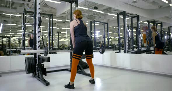 Athletic Girl in the Gym Doing Standing Exercises with a Barbell on His Back, Makes a Deadlift alt
