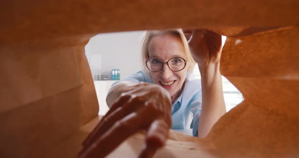 View From Inside Paper Bag of Mature Businesswoman Taking Croissant and Eating alt