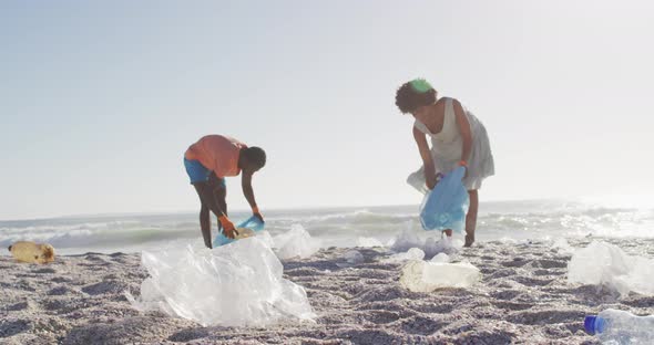 African american couple segregating waste together on dirty sunny beach alt