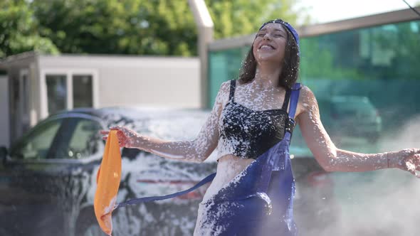 Cheerful Woman Laughing As Water Spraying Washing Off Car Wash Shampoo in Slow Motion alt