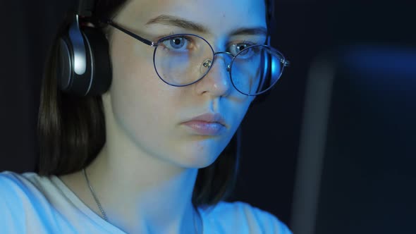 Closeup Portrait of Teenage Girl with Glasses and Wireless Headphones Looks at the Monitor alt
